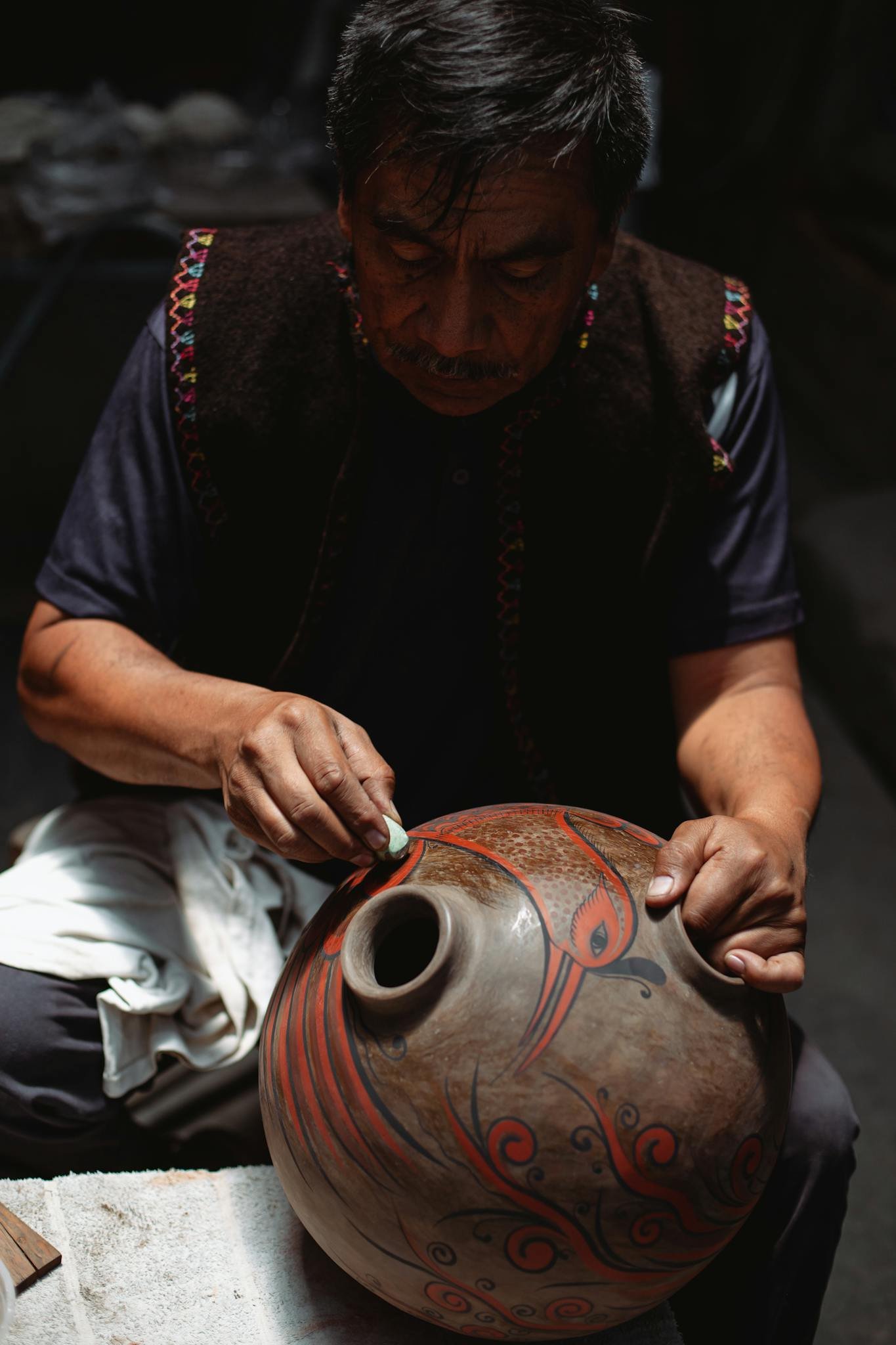 A skilled artisan hand-paints intricate designs on a traditional Mexican pottery piece in a workshop setting.
