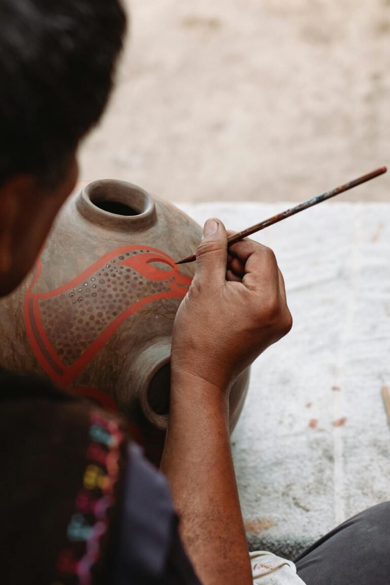 Close-up of artisan painting a ceramic pot with intricate patterns in a workshop.