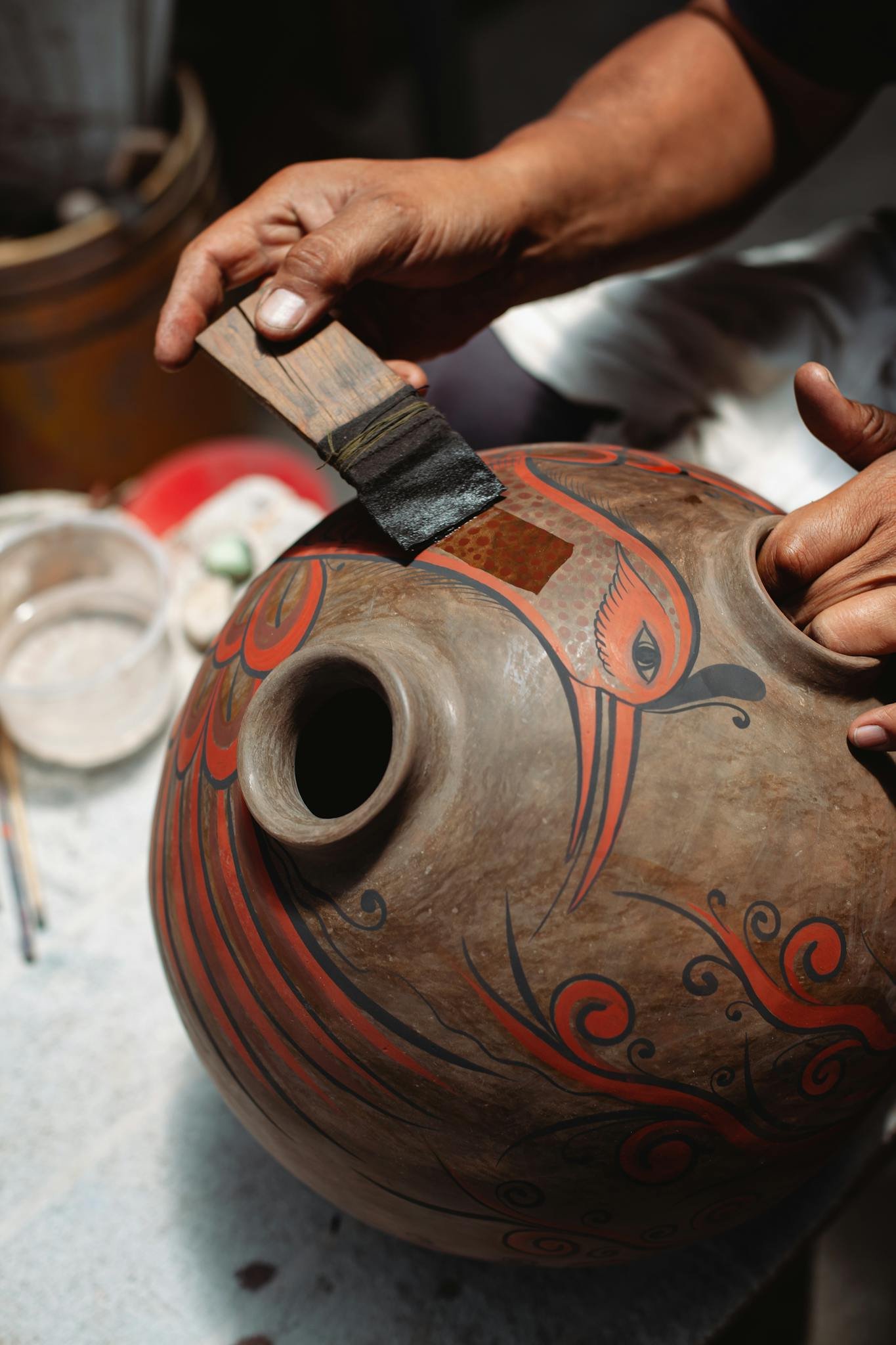 Close-up of hands painting intricate designs on a traditional ceramic pot, showcasing artisan craftsmanship.